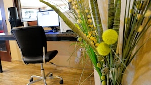 Ein Schreibtisch mit einem Computer, einem schwarzen Bürostuhl und einer Vase mit gelben Blumen.