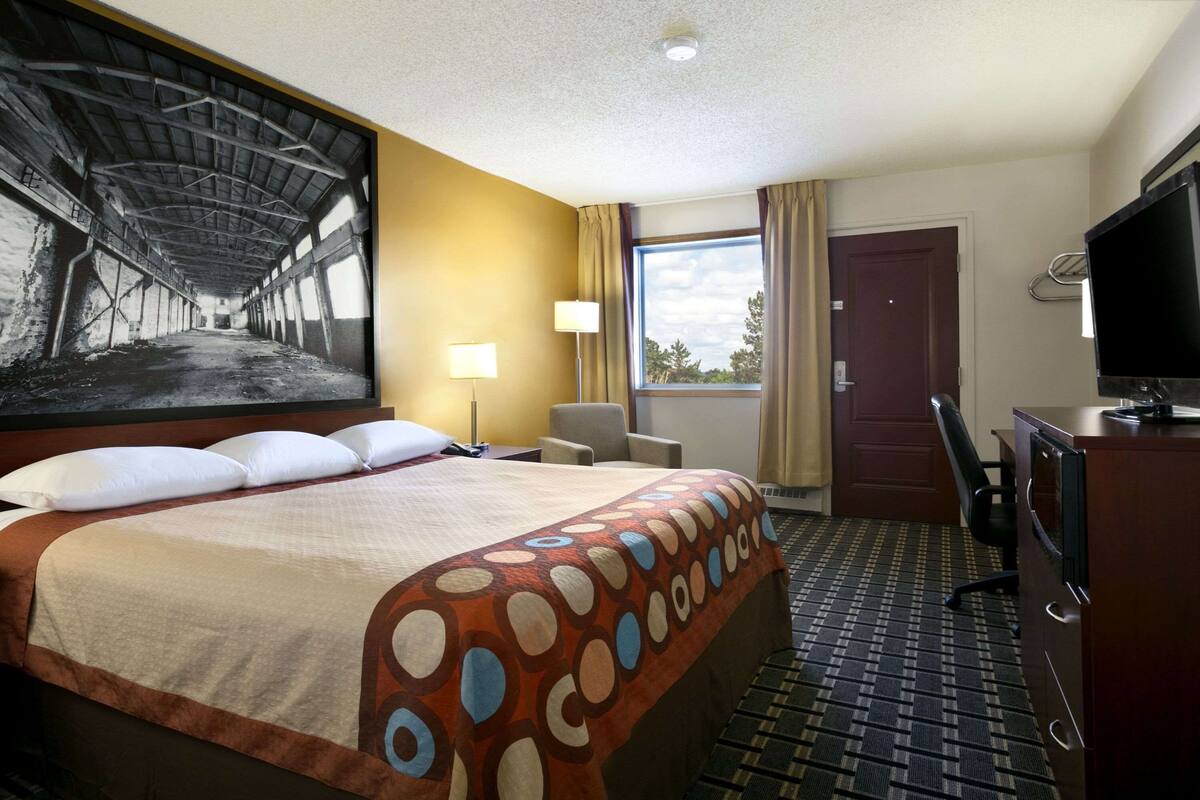 Habitación de hotel con una cama grande, un escritorio, un televisor y una ventana con cortinas.