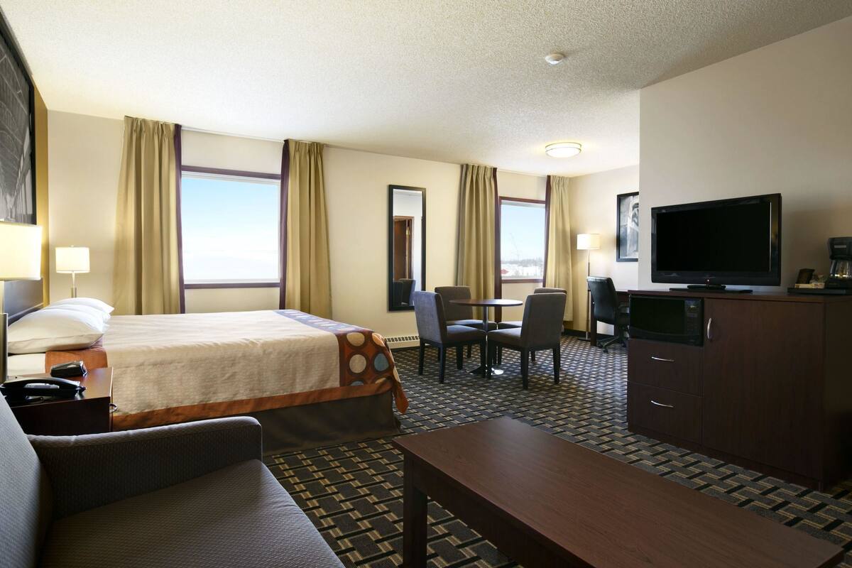 Una habitación de hotel con cama, escritorio con silla, televisor y cafetera.