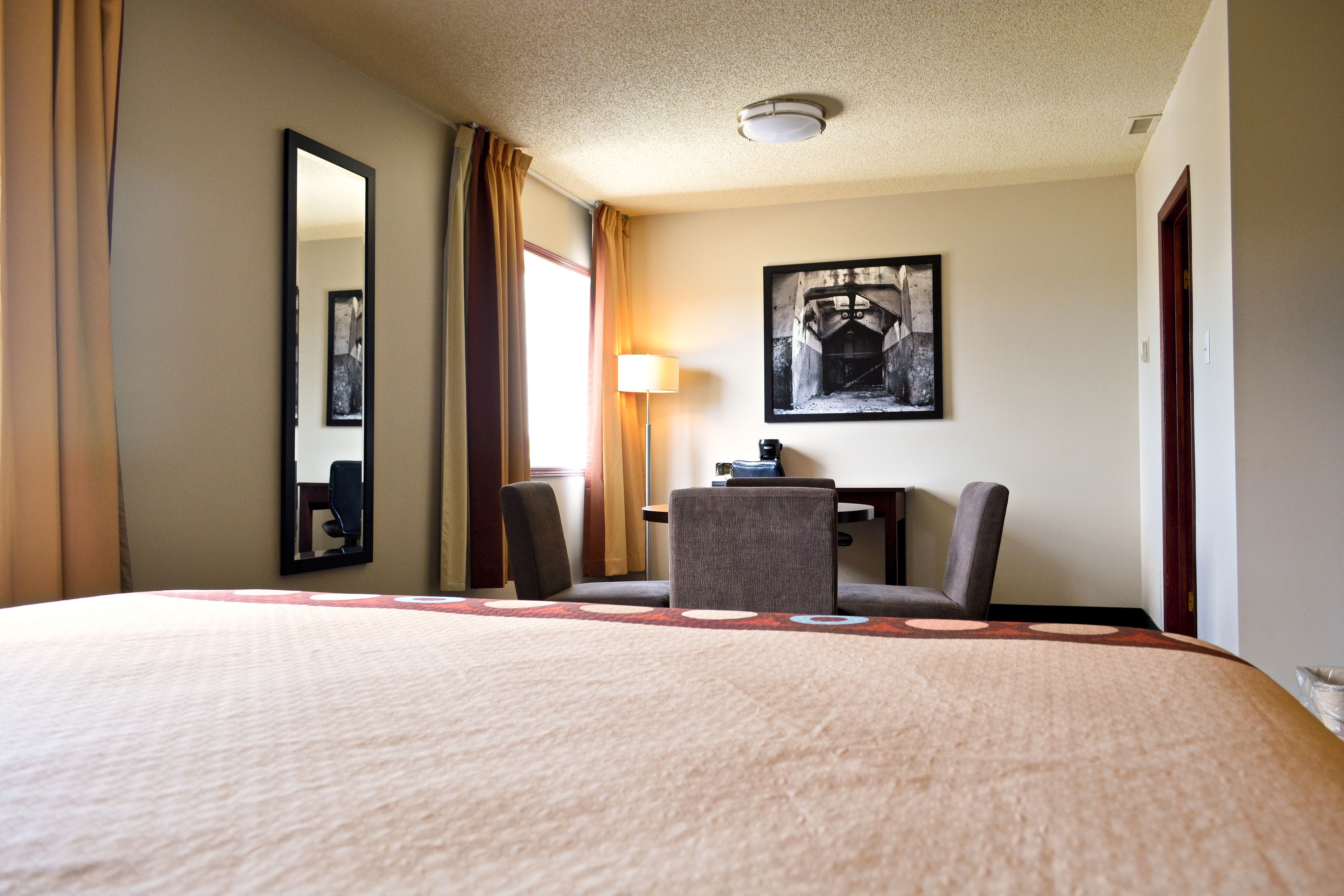 Habitación de hotel con una cama grande, un escritorio, dos sillas, una lámpara y un cuadro en la pared.