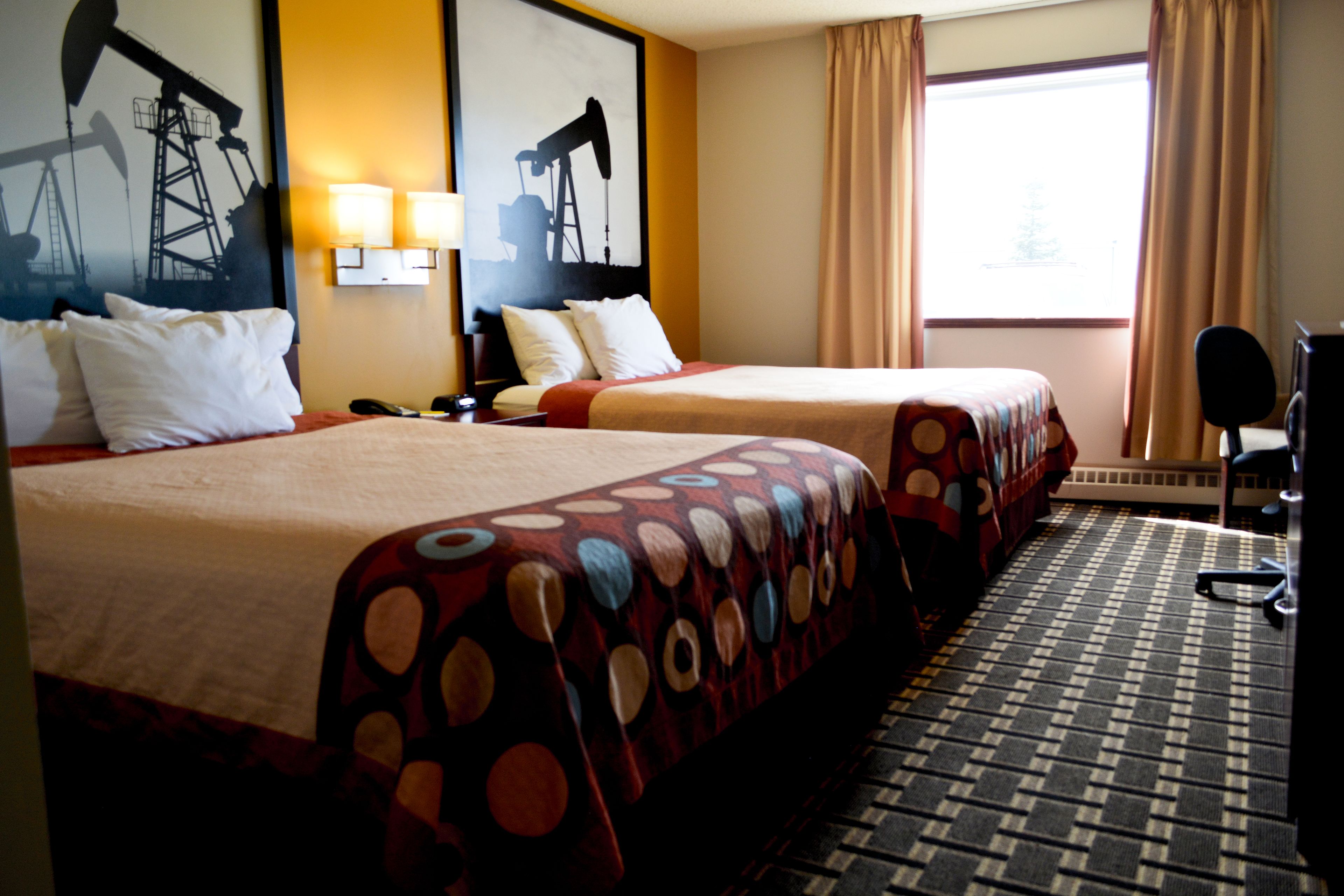 A hotel room with two beds, a desk, a chair, and artwork on the walls.