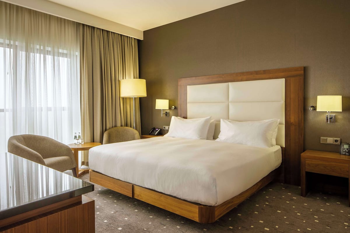 A hotel room with a large bed, two bedside tables with lamps, a chair, and a desk.