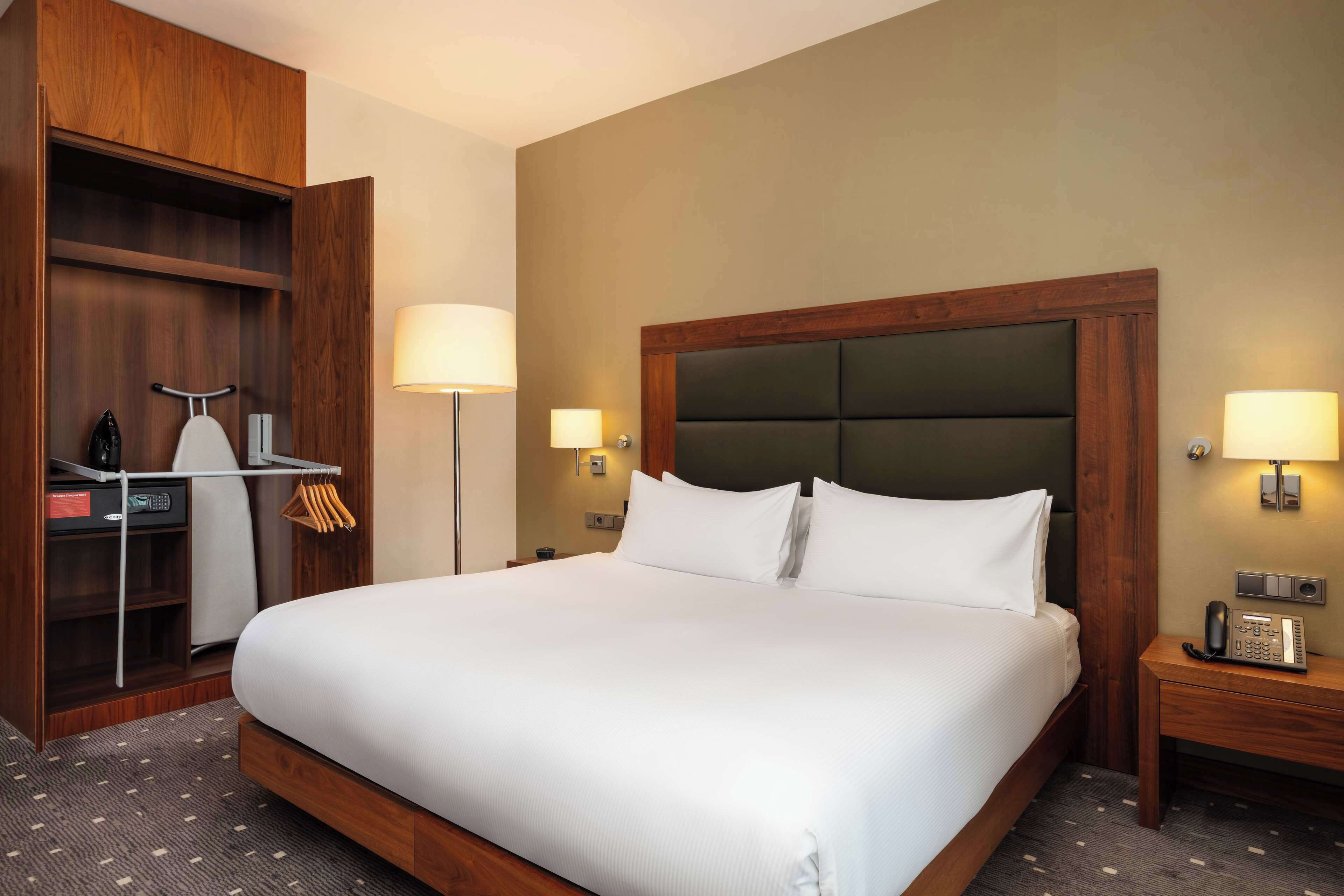 Une chambre d’hôtel avec un grand lit, une armoire en bois, des lampes de chevet et un bureau avec un téléphone.