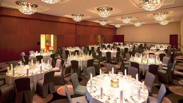 Un salón de banquetes con varias mesas redondas dispuestas para comer, cada una con sillas y centros de mesa.