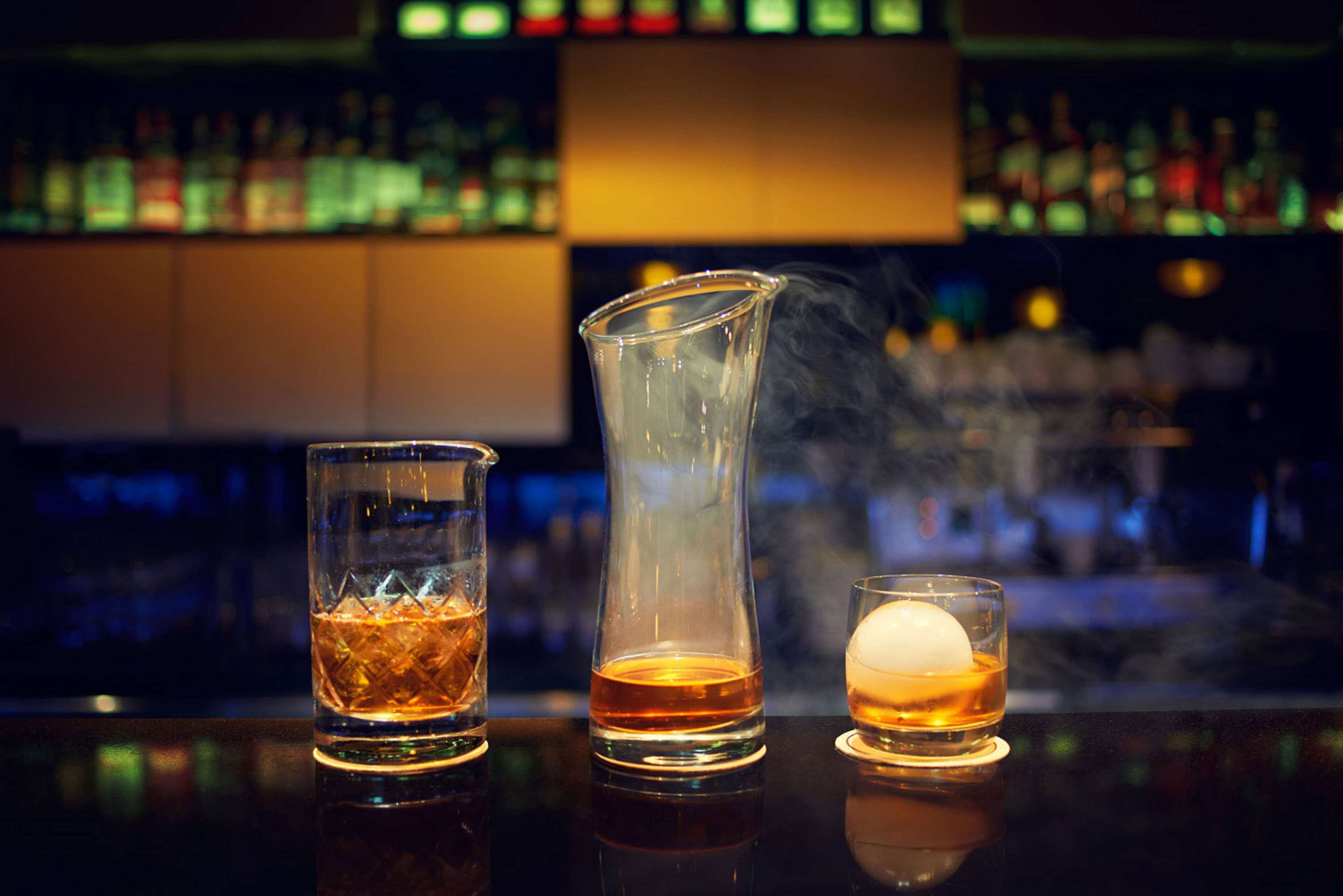 Three glasses of whiskey on a bar counter with a blurred background of shelves with bottles.