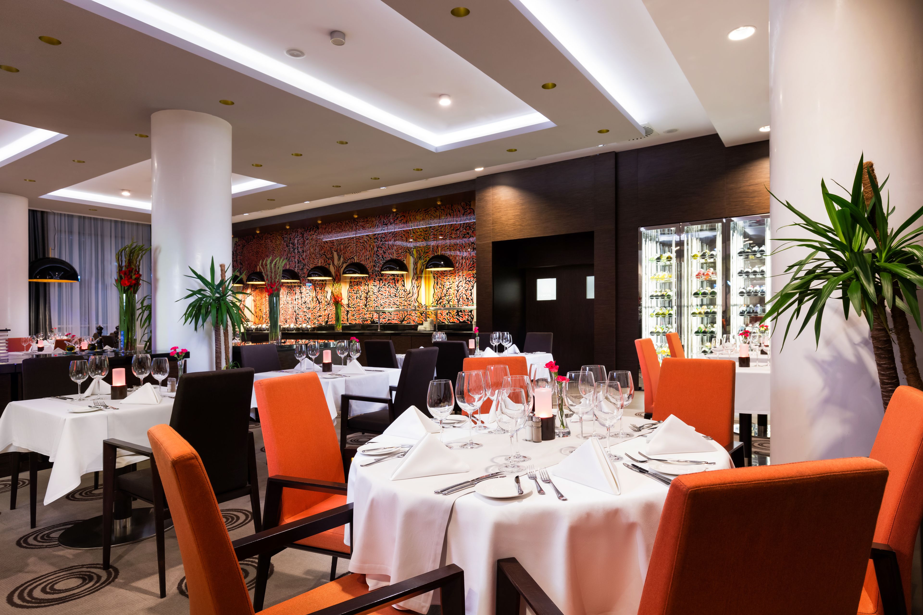 A restaurant with white tablecloths, orange chairs, and a modern ceiling design.