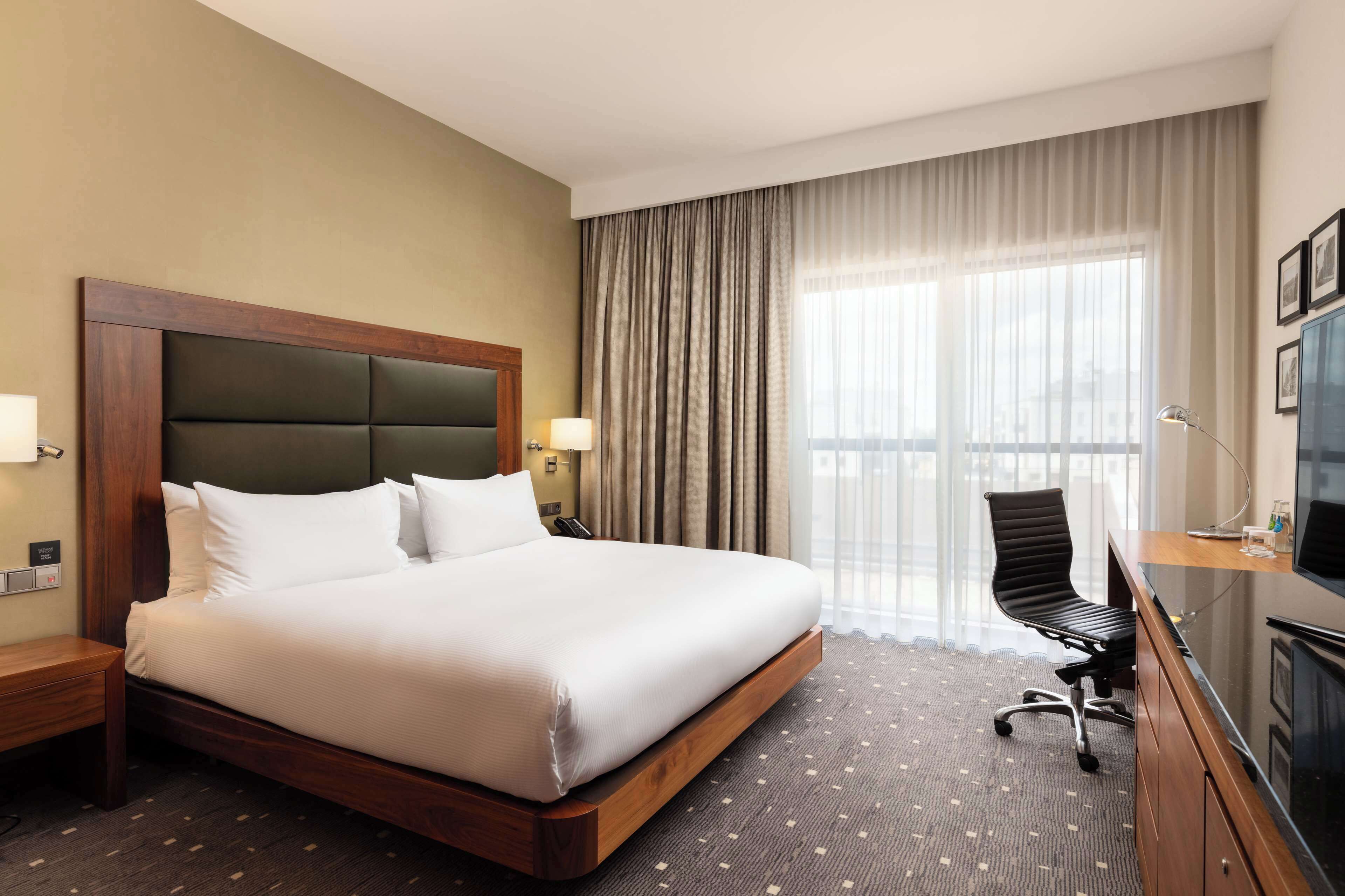 Una habitación de hotel con una cama grande, un escritorio con silla, un televisor y una ventana con cortinas.