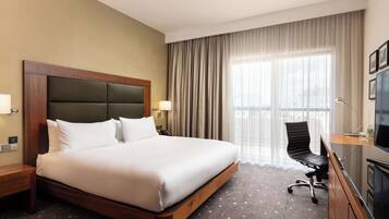 Una habitación de hotel con una cama grande, un escritorio con silla, un televisor y una ventana con cortinas.