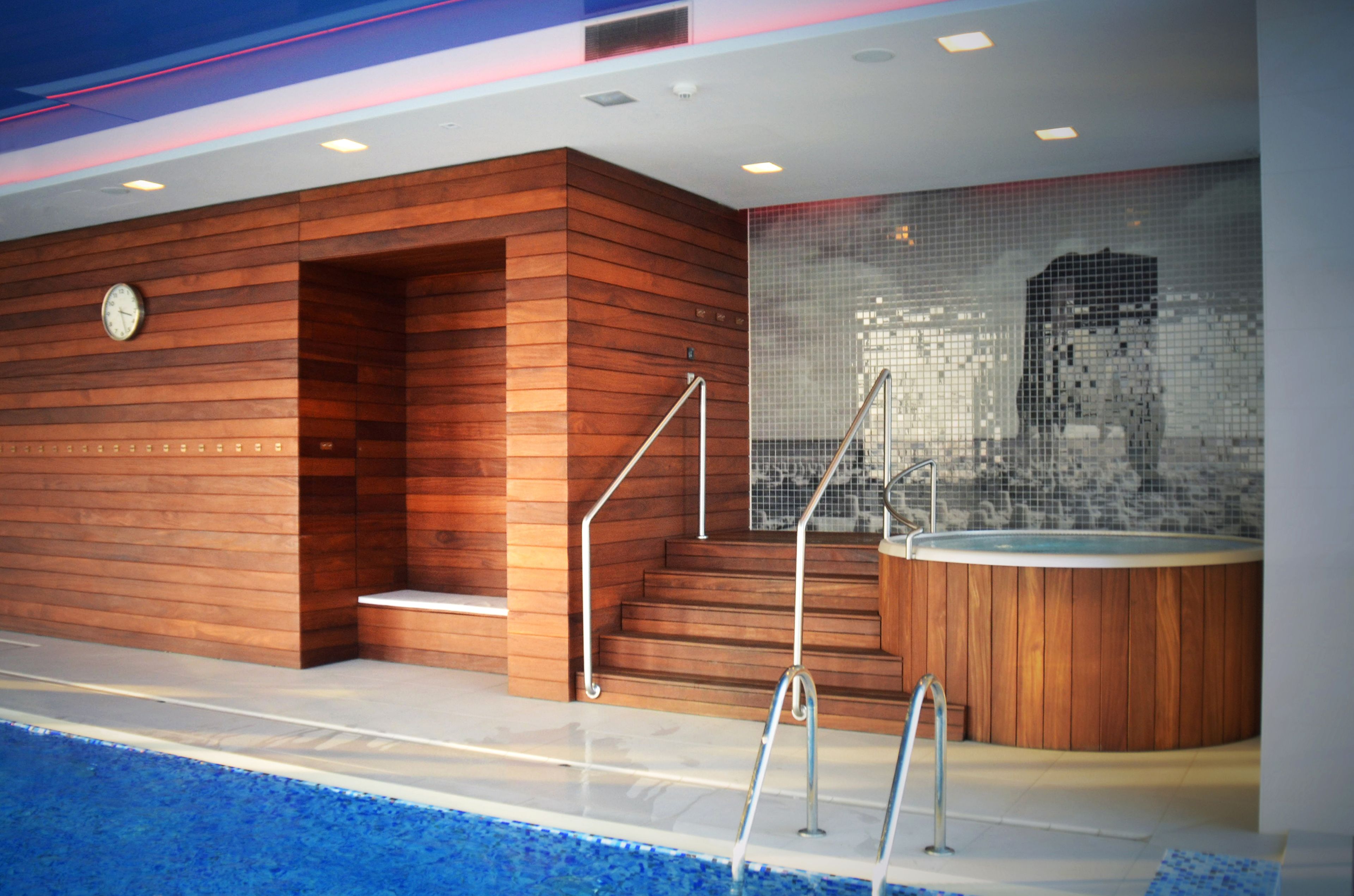 Un área de piscina interior moderna con paredes de madera, un jacuzzi y un muro decorado con mosaicos.