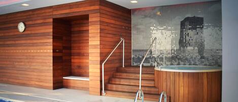 Un área de piscina interior moderna con paredes de madera, un jacuzzi y un muro decorado con mosaicos.