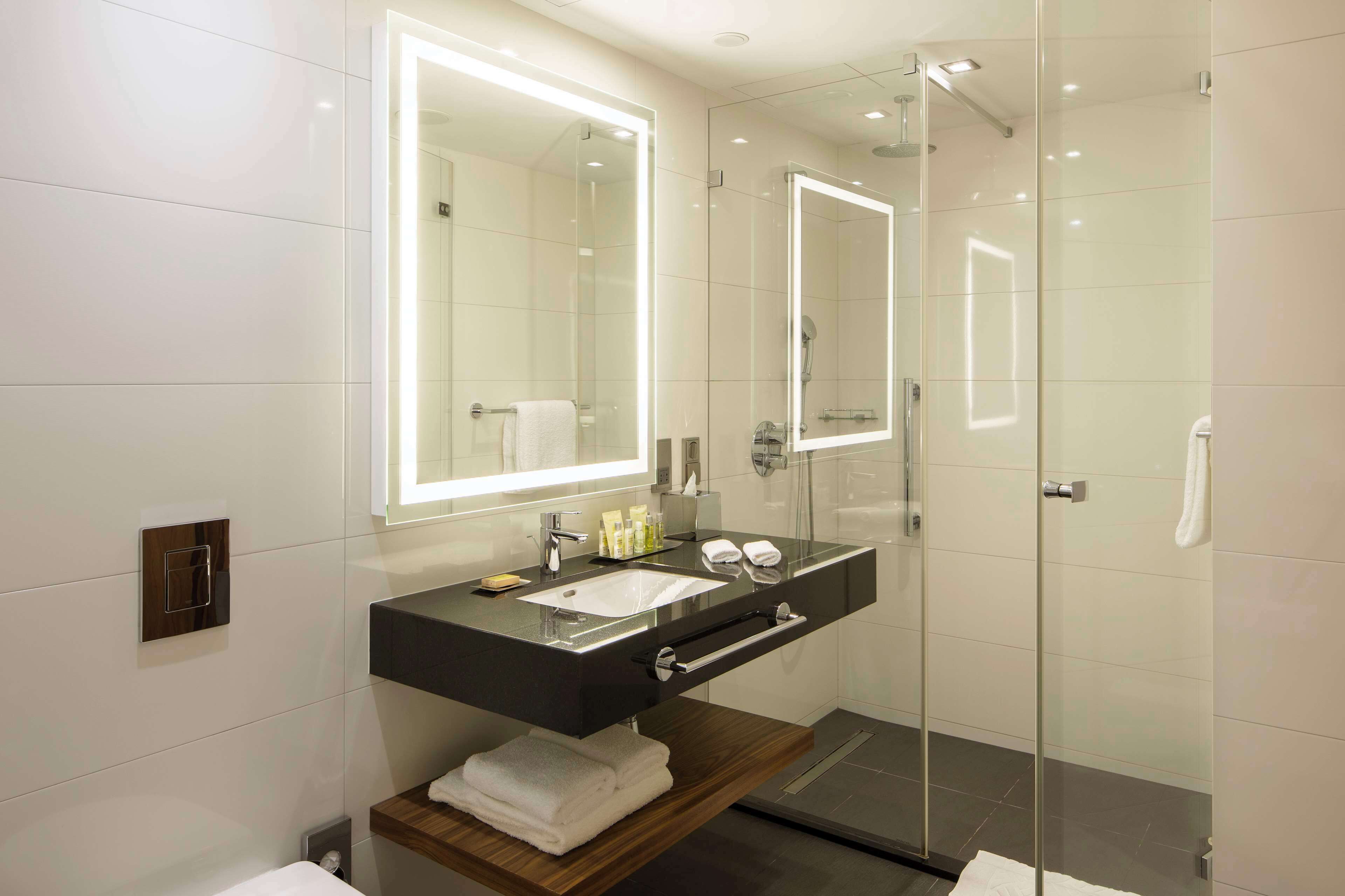 Une salle de bain moderne dotée d’une douche à parois de verre, d’un grand miroir et d’un meuble-lavabo avec un évier et un porte-serviettes.