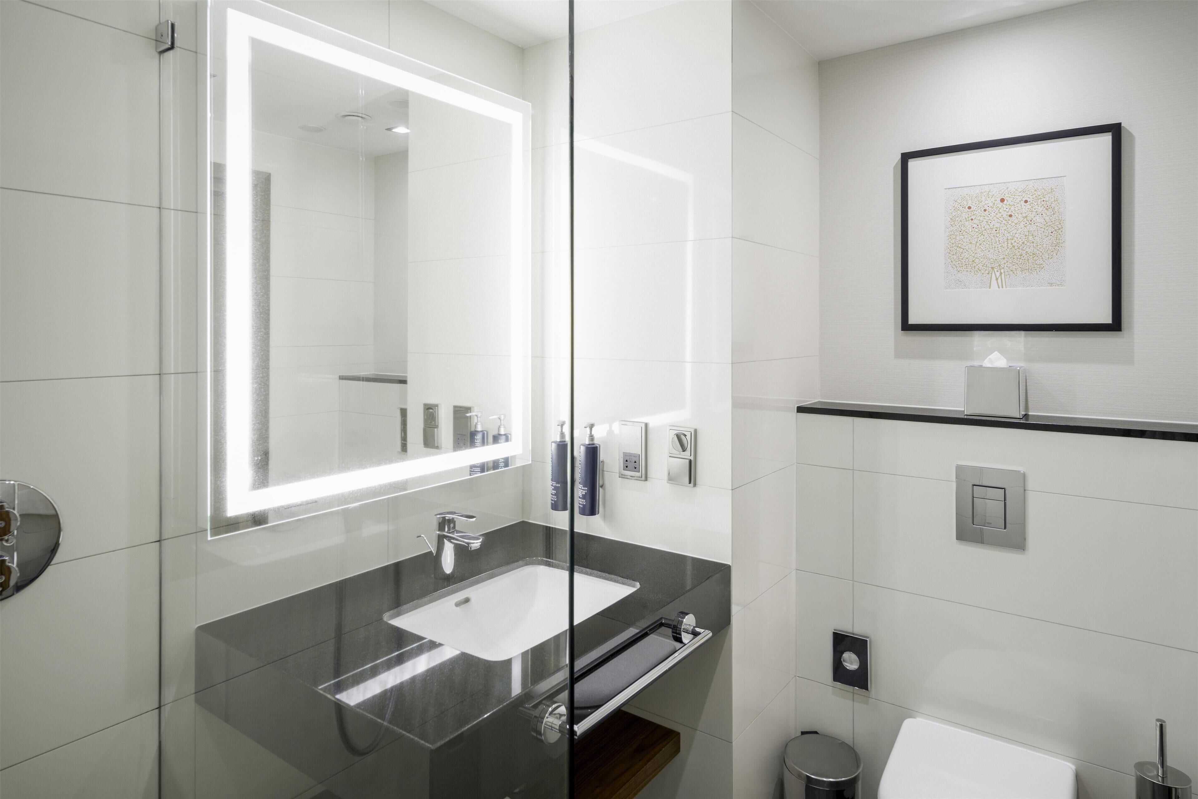A modern bathroom with a glass-enclosed shower, a white sink, and a framed artwork on the wall.