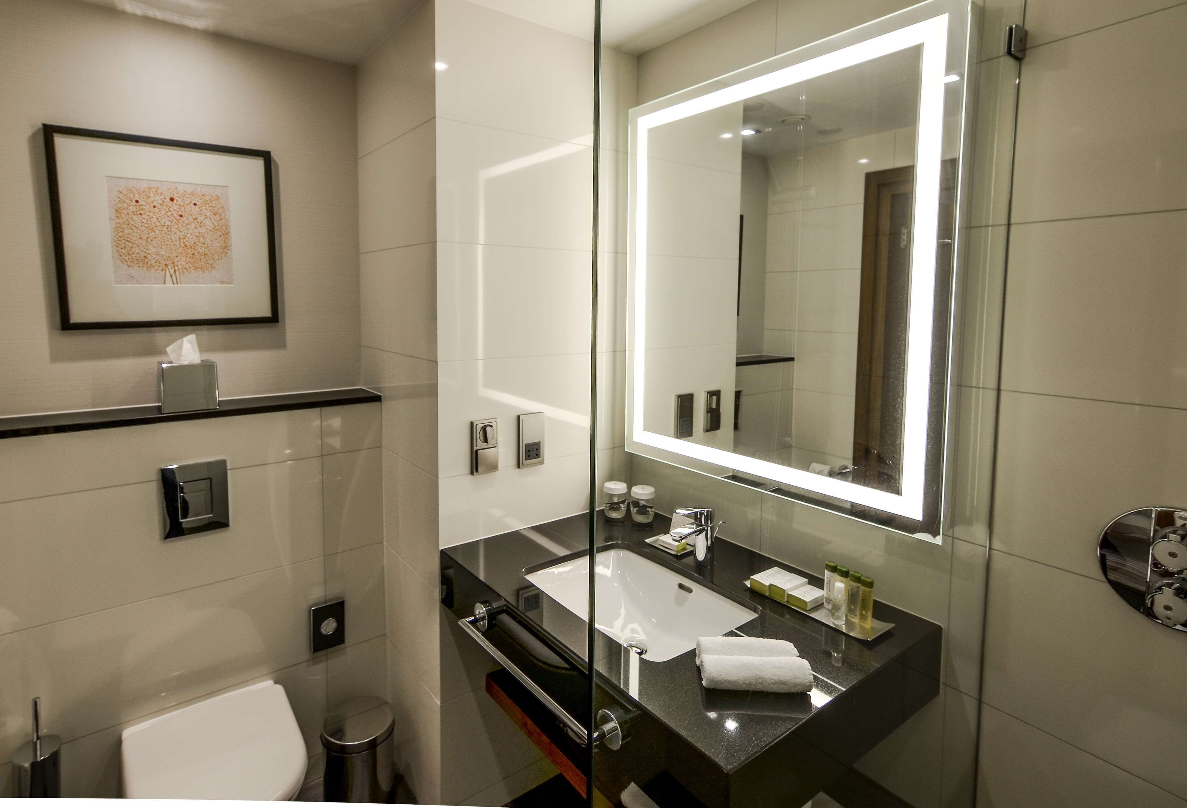 Un bagno moderno con doccia vetrata, uno specchio grande, un lavandino bianco e un'opera d'arte incorniciata al muro.