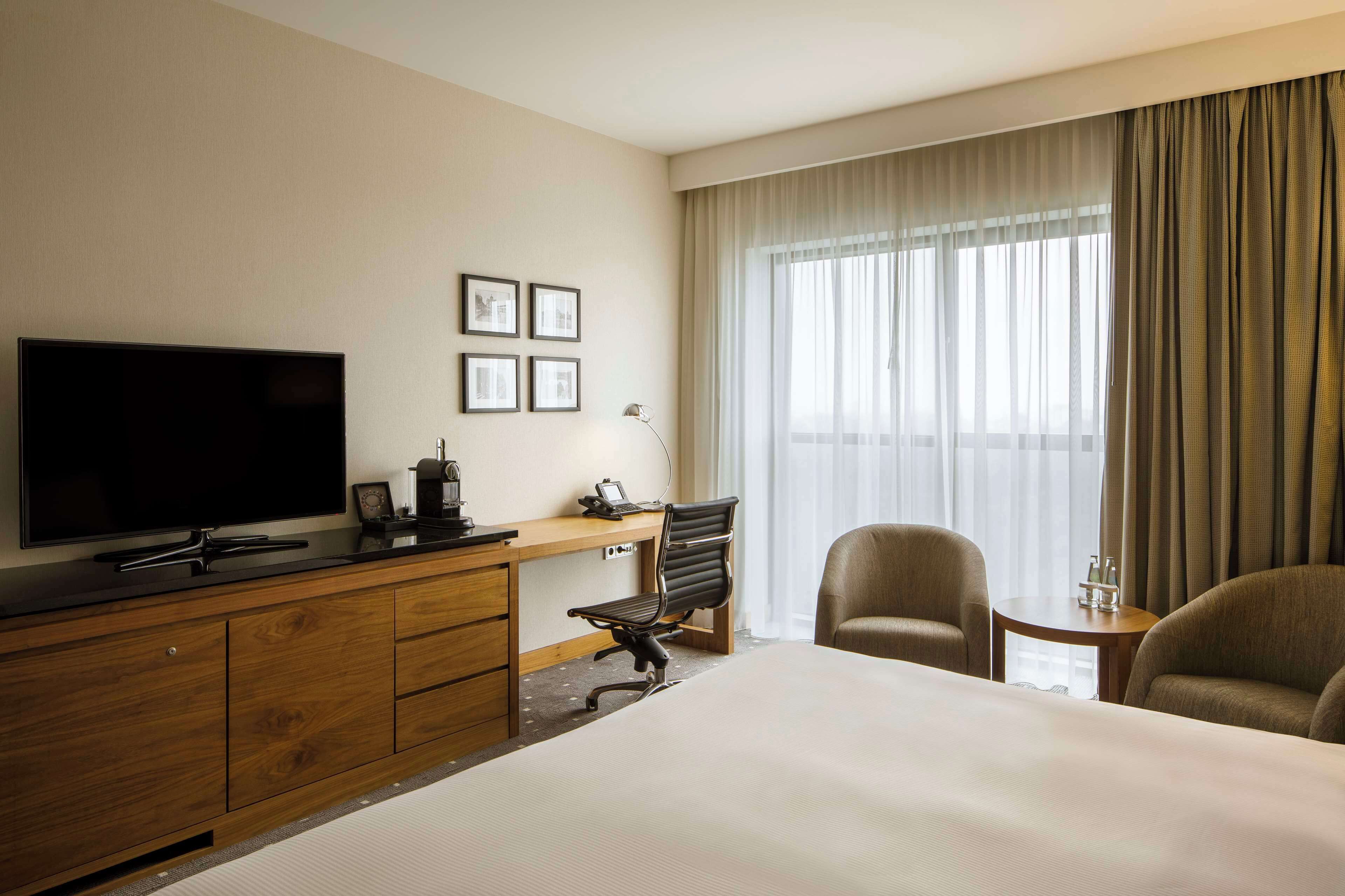 A hotel room with a large bed, a desk with a computer, a television, and a chair.