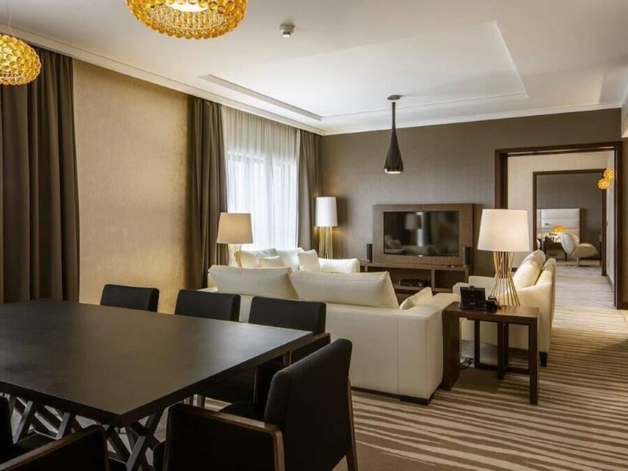 Et moderne hotelværelse med spiseplads, en sofa, et fjernsyn og en lampe.