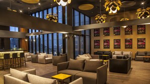 Un área de lounge moderna con sofás, bar y grandes ventanales con vistas a la ciudad.
