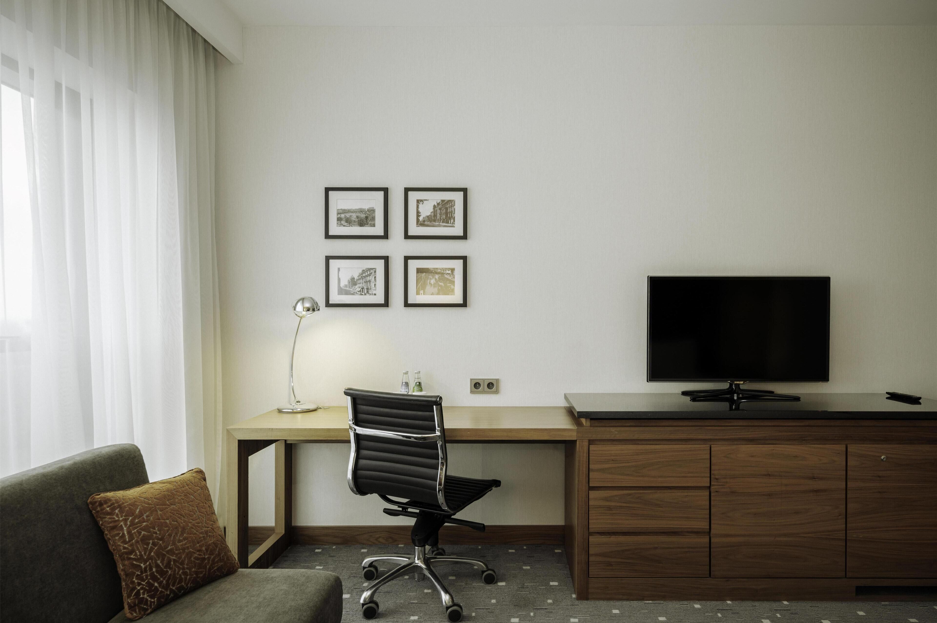 Habitació d'hotel amb escriptori, cadira, televisió i sofà.