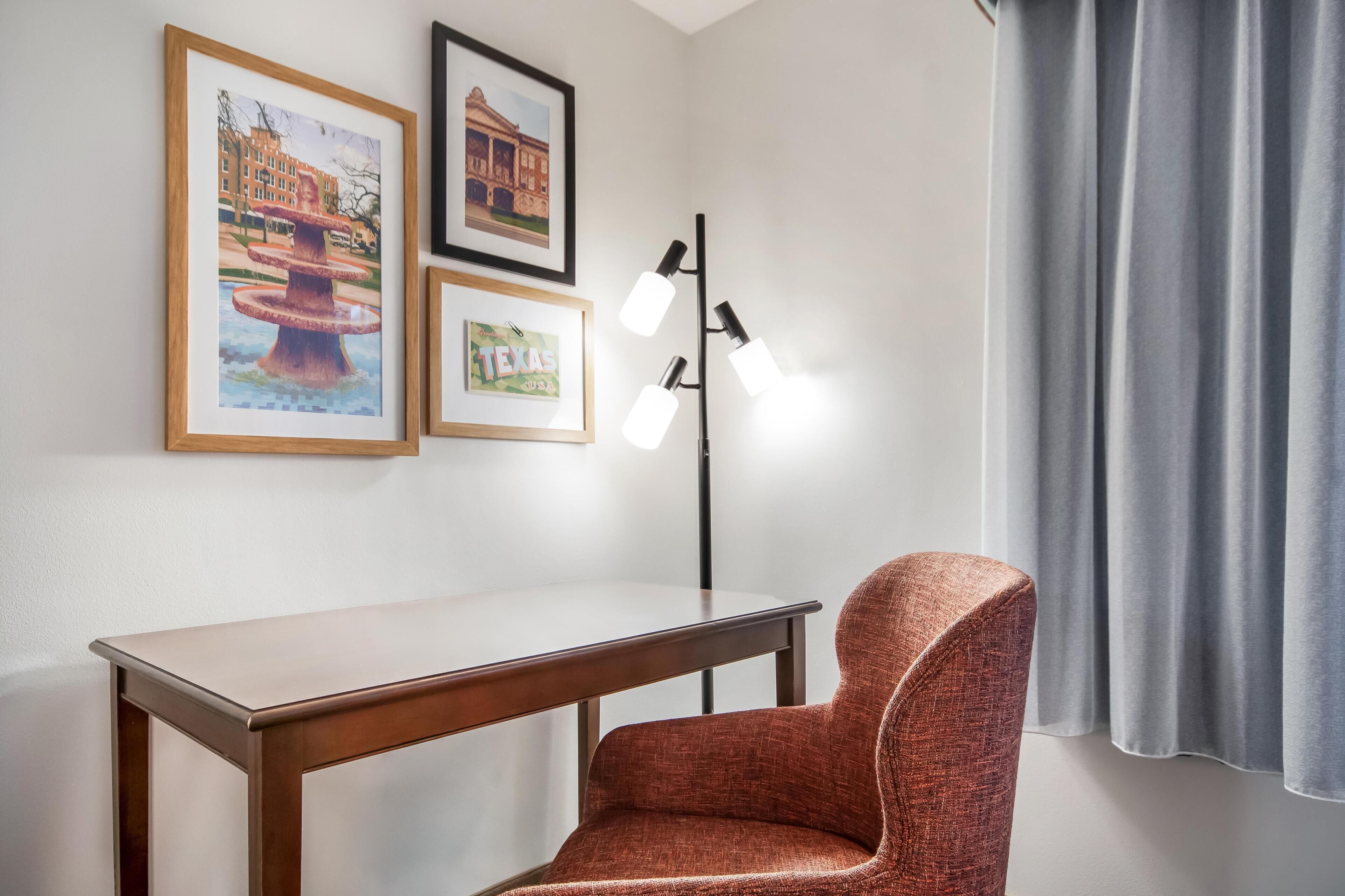 Une pièce avec un bureau en bois, une chaise rembourrée de couleur rouge, un lampadaire et des tableaux encadrés accrochés au mur.