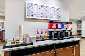 Una estación de café con varios dispensadores, un menú de café y una pared con iconos de bebidas.
