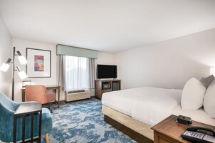 Habitación de hotel con una cama grande, un escritorio con silla, un televisor y un teléfono.