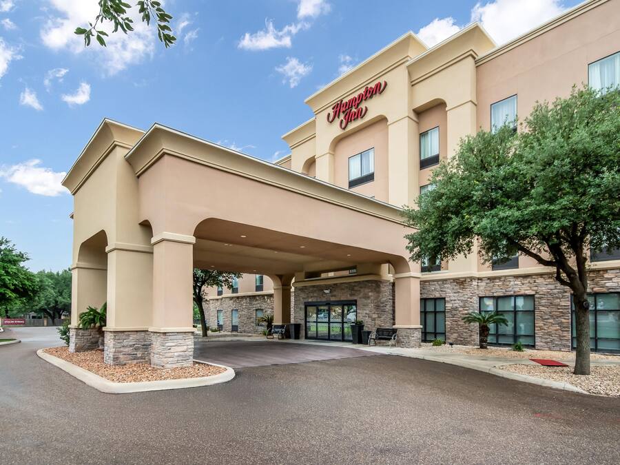 Un Hampton Inn amb entrada coberta, façana de pedra i un cel blau clar.