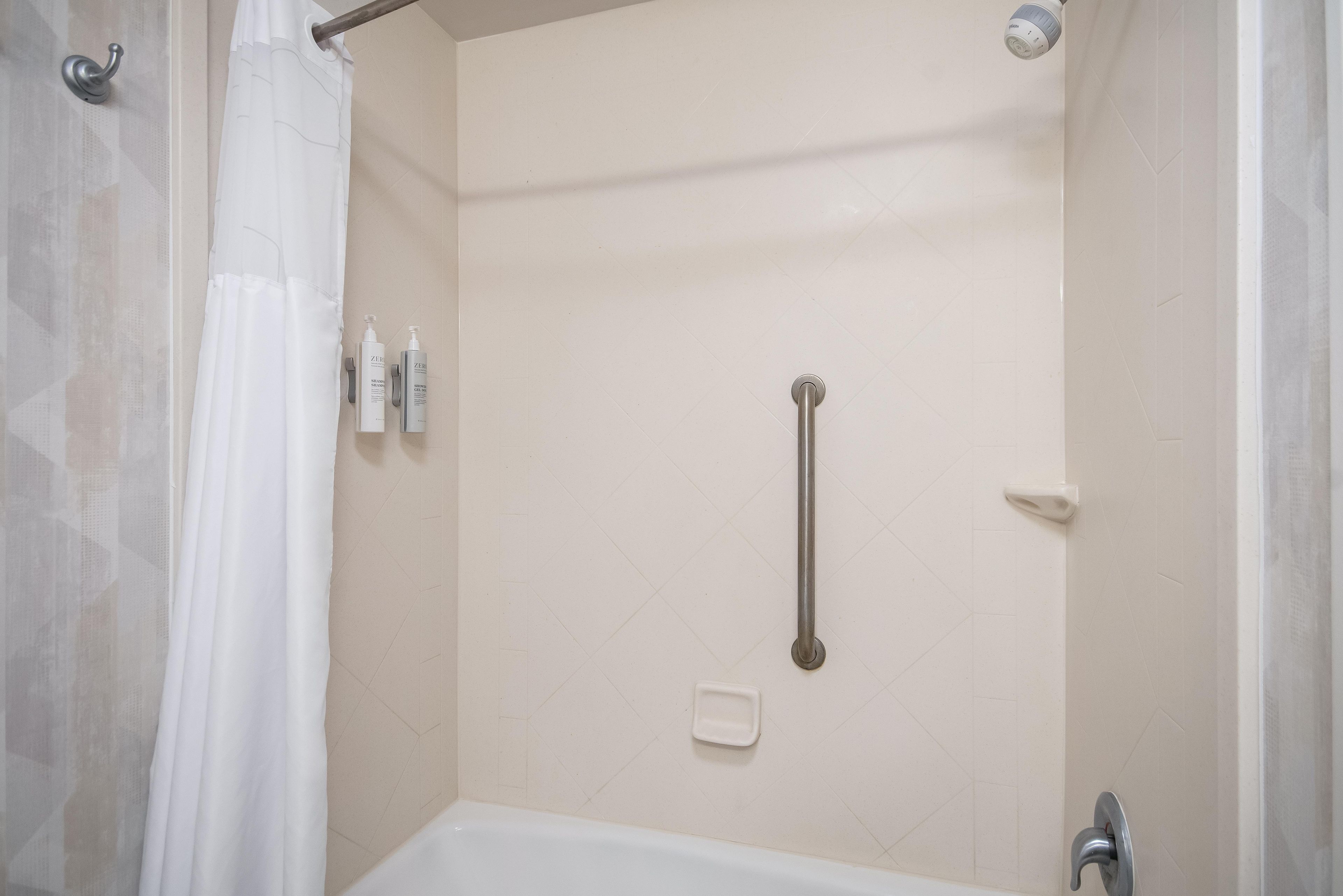 Ducha con barra de apoyo, bañera blanca y cortina de ducha.