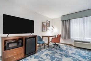 A hotel room with a flat-screen TV, a microwave, a mini-fridge, a desk, two chairs, and a large window with curtains. - Hampton Inn Uvalde (Uvalde)