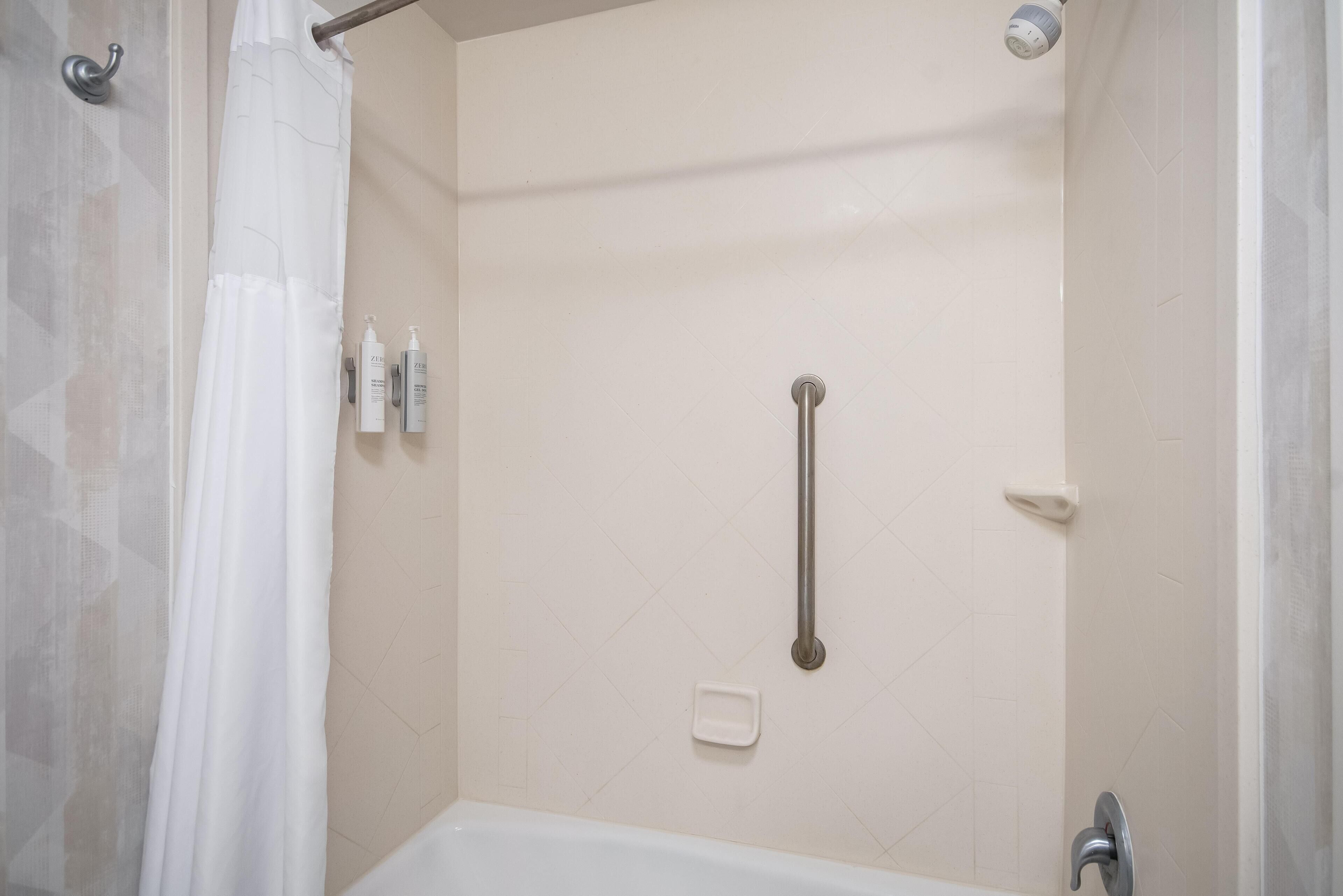 Ducha con barra de apoyo, bañera blanca y cortina de ducha.