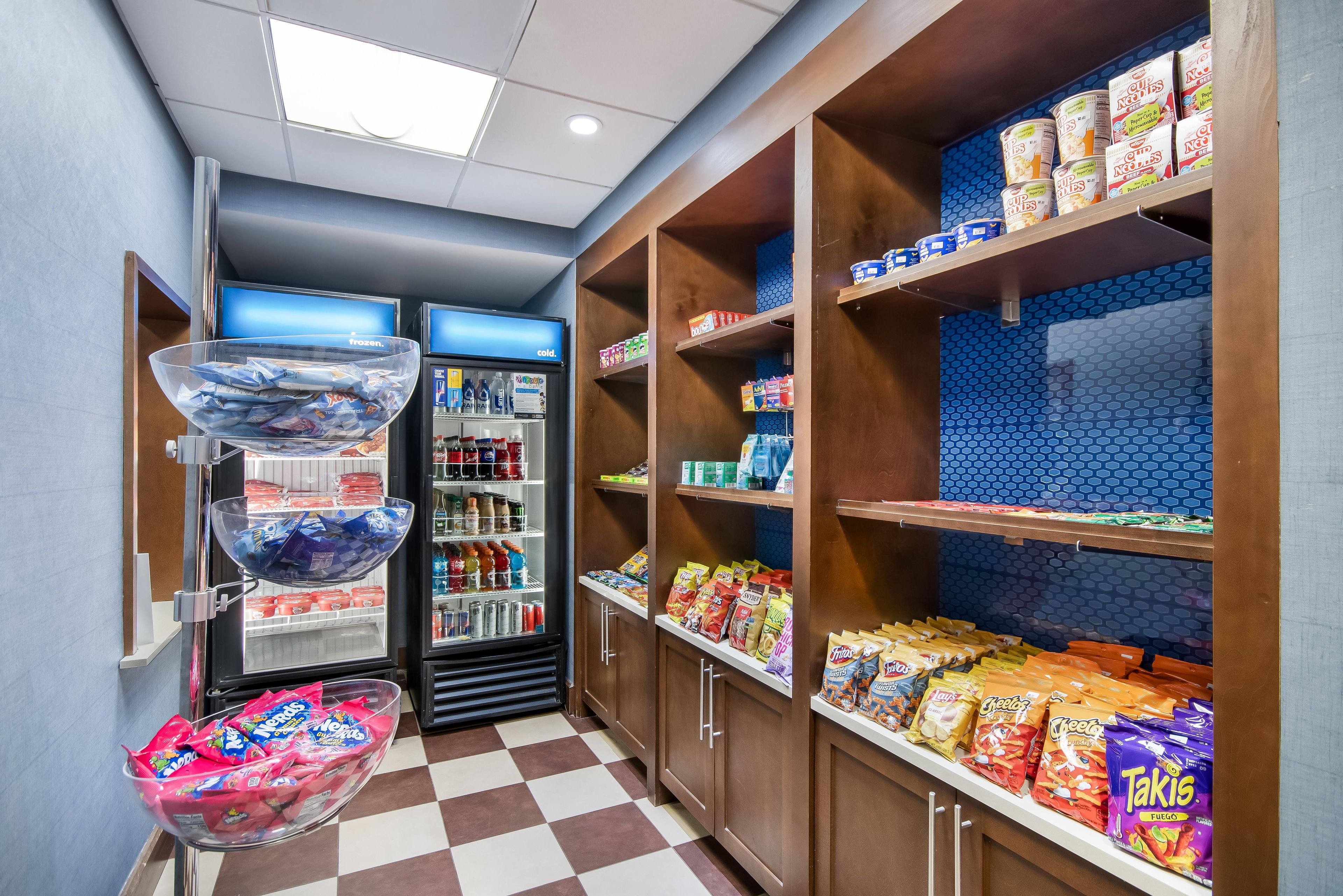 Un bar con un banco frigo, scaffali pieni di snack e un pavimento a scacchi.