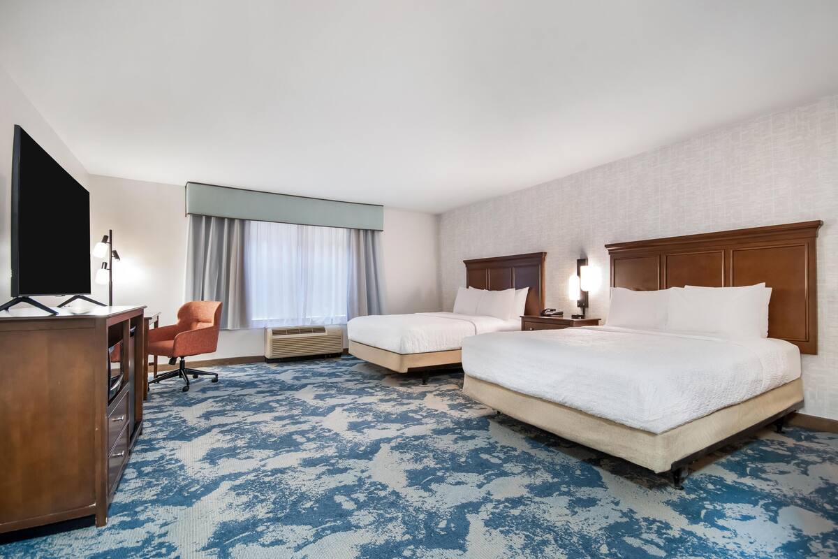 A hotel room with a large bed, a smaller bed, a desk, a chair, and a TV.