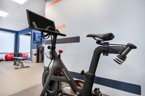An indoor gym with exercise equipment, a Peloton stationary bike, and a wall-mounted screen. - Hampton Inn Uvalde (Uvalde)