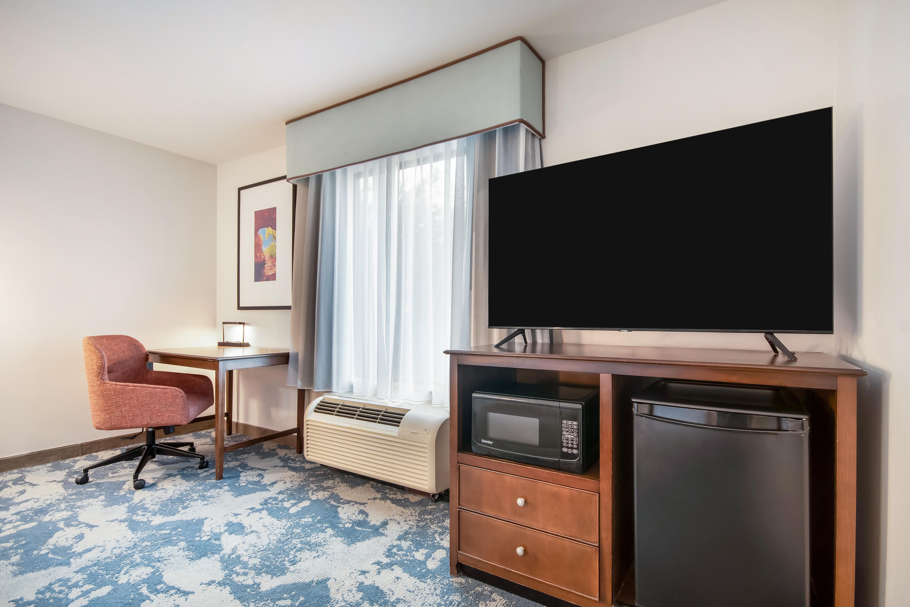 Une chambre d’hôtel équipée d’un bureau, d’une chaise, d’une télévision à écran plat, d’un four à micro-ondes et d’un mini-réfrigérateur.