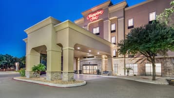 A Hampton Inn hotel with a stone facade, a prominent neon sign, and a covered entrance area.