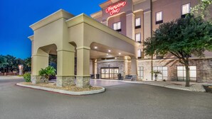 A Hampton Inn hotel with a stone facade, a prominent neon sign, and a covered entrance area.