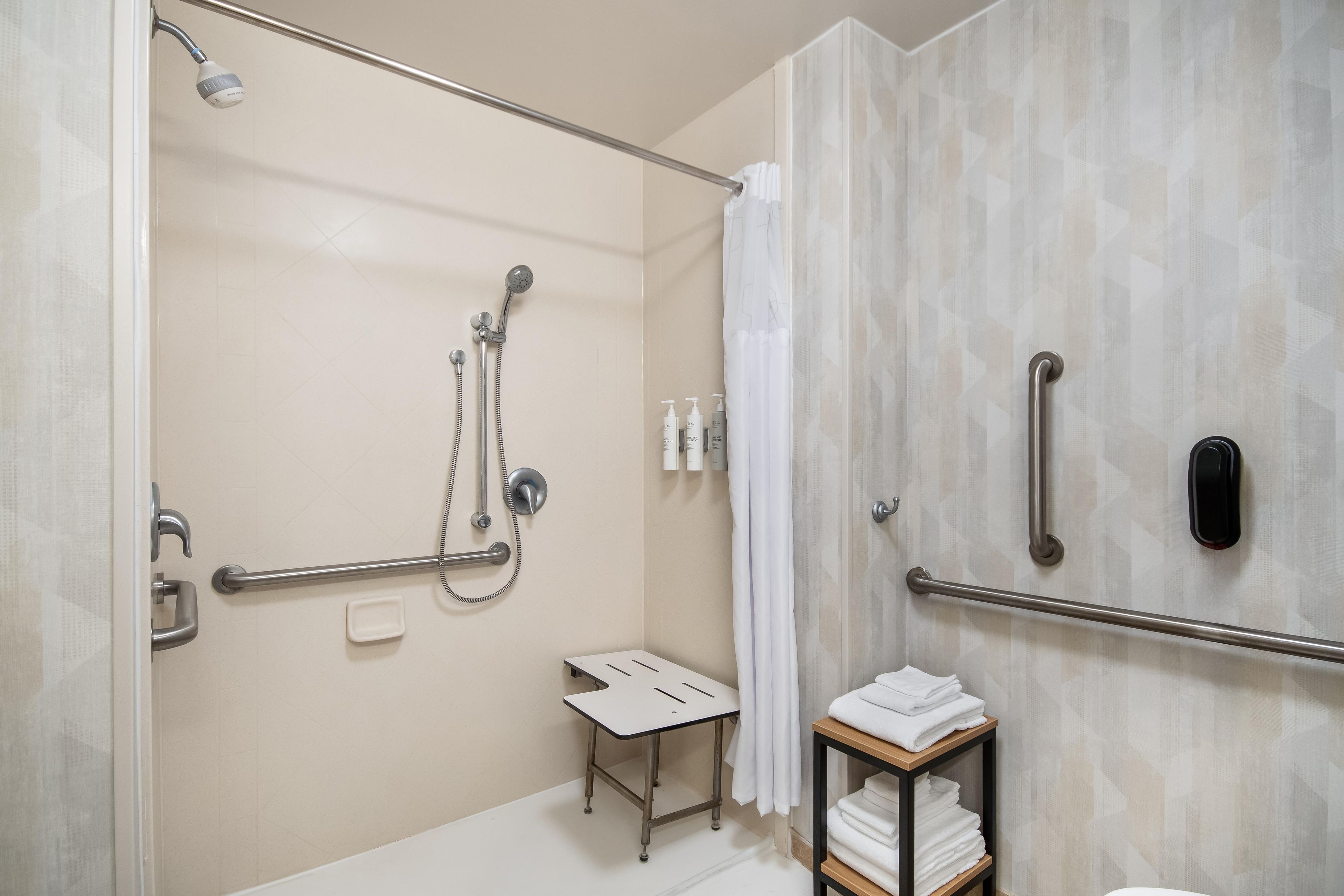 Ein modernes Badezimmer mit Dusche, Haltegriffen, einem Handtuchhalter und einem kleinen Tisch.