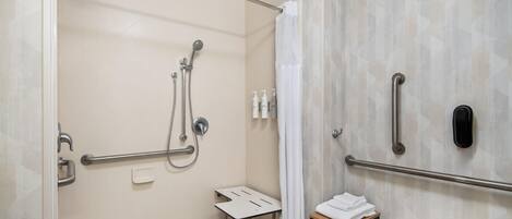 Ein modernes Badezimmer mit Dusche, Haltegriffen, einem Handtuchhalter und einem kleinen Tisch.