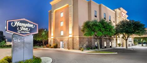 A Hampton Inn by Hilton hotel with a well-lit entrance, a signboard, and a parking area.