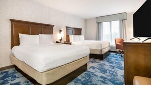 A hotel room with two beds, a desk, a chair, a TV, and a large window with curtains.