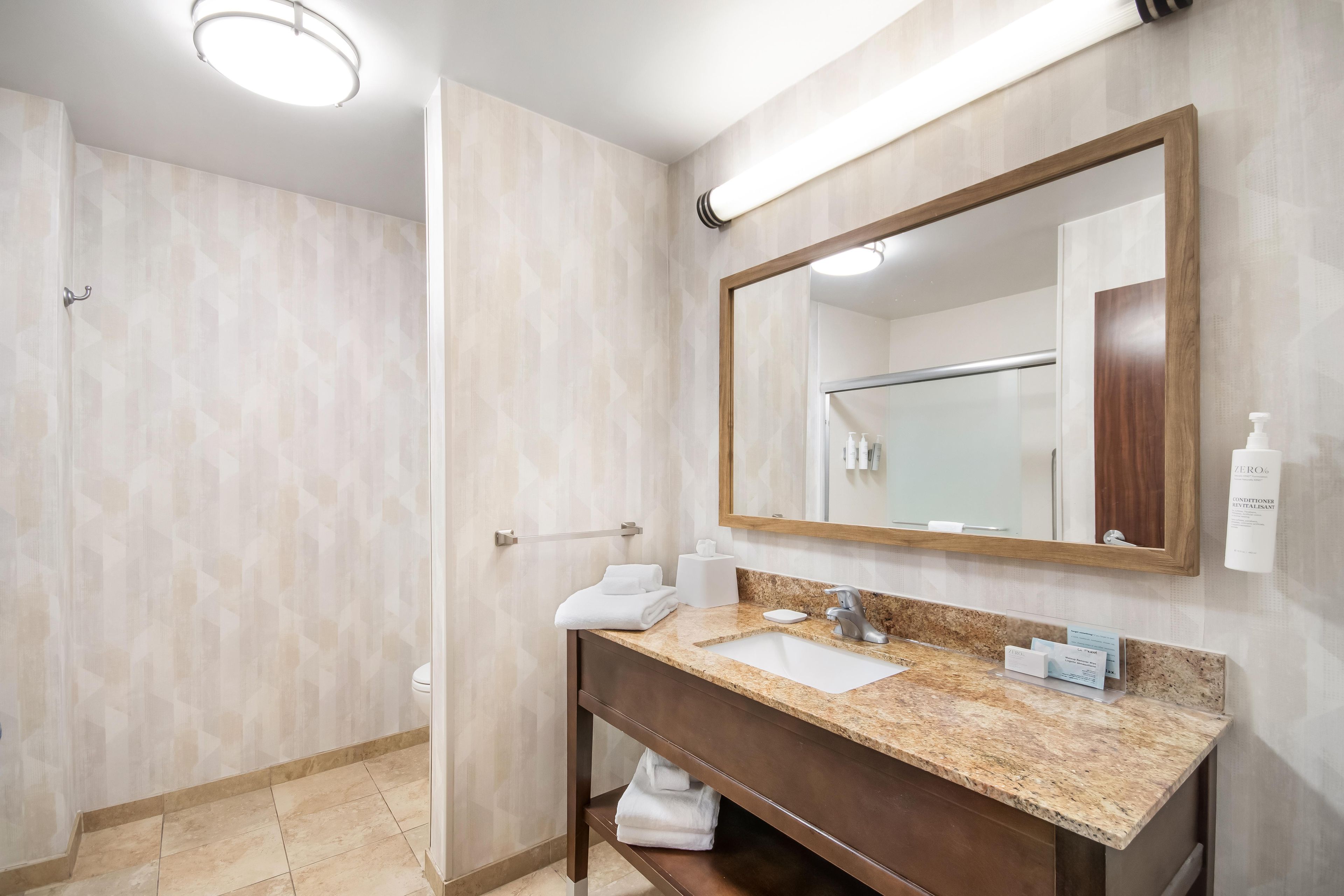 A bathroom with a sink, mirror, towel rack, and shower area.