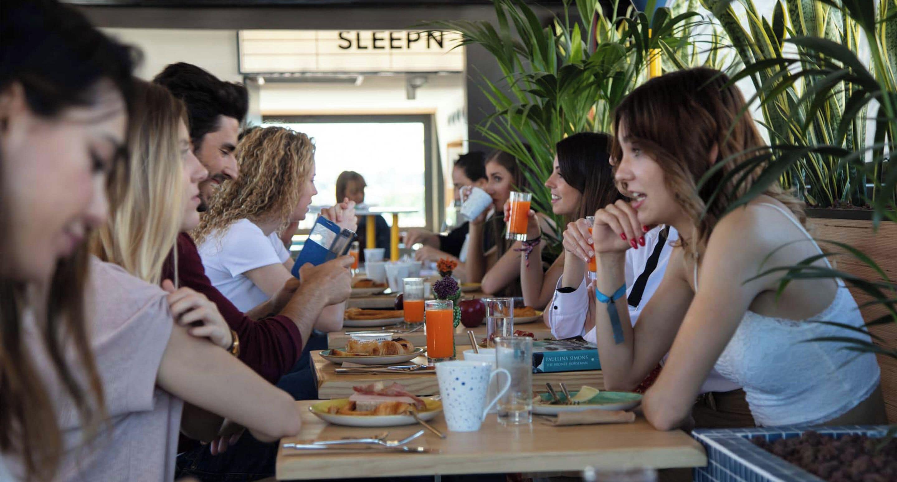 A group of people dining at a table with breakfast items and drinks, in a room with a sign that reads 'SLEEPN'.