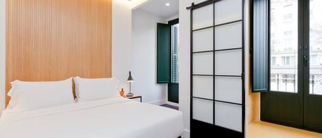 Habitación de hotel moderna con una cama grande, una puerta corredera con paneles de vidrio esmerilado y vistas de la ciudad a través de la puerta.