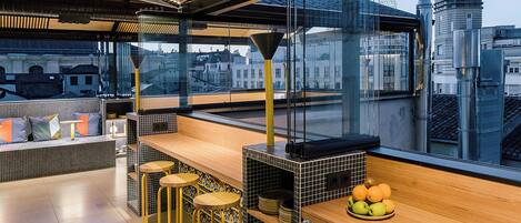 Zona de bar moderna con mostrador de madera, taburetes y vistas a la ciudad a través de amplias ventanas.