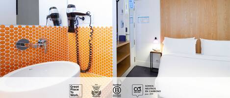 A modern bathroom with a large sink and two hair dryers, and a bedroom with a wooden headboard and a bed.