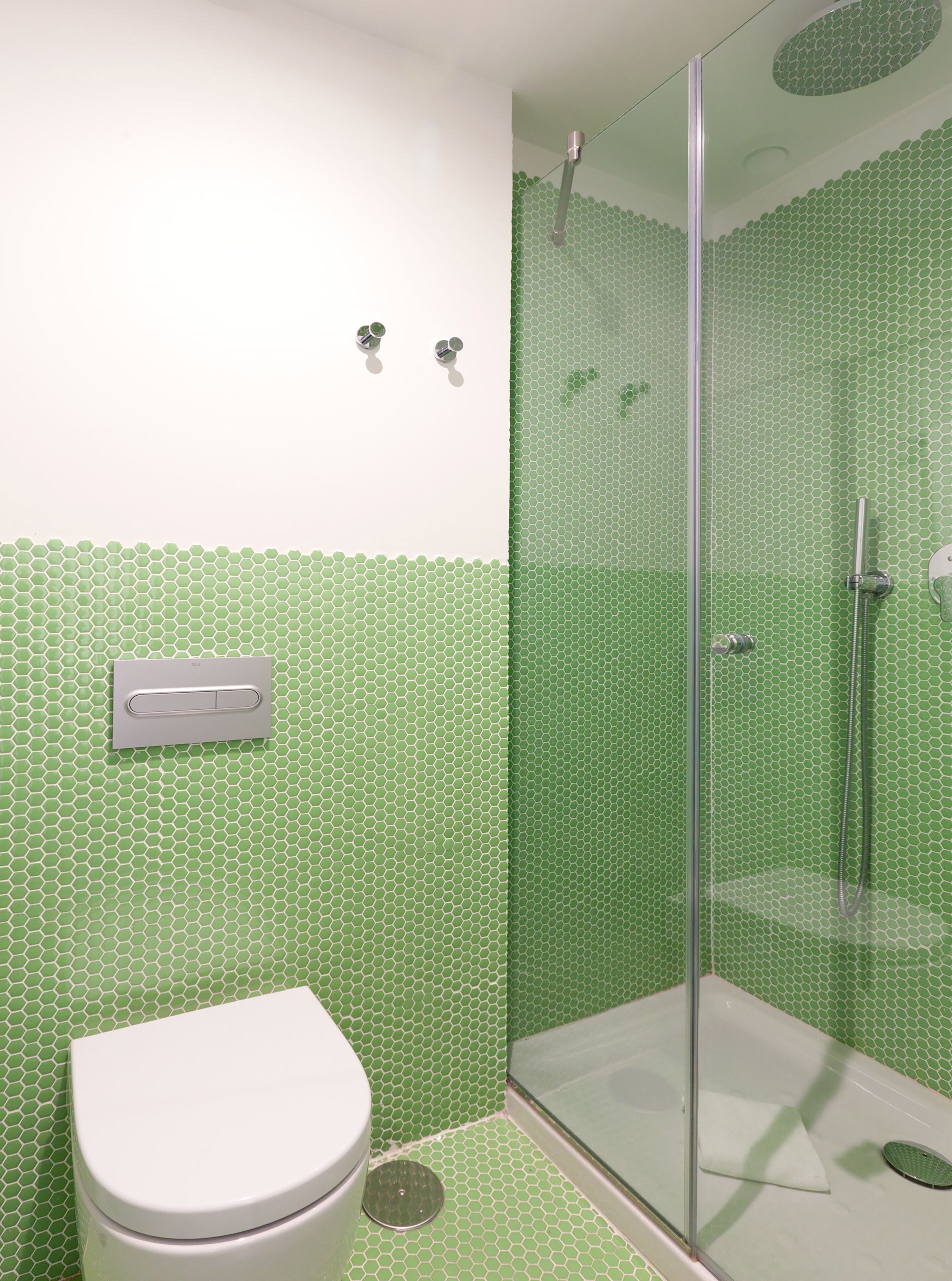 Un baño con inodoro, ducha con puerta de cristal y pared de azulejos hexagonales verdes.