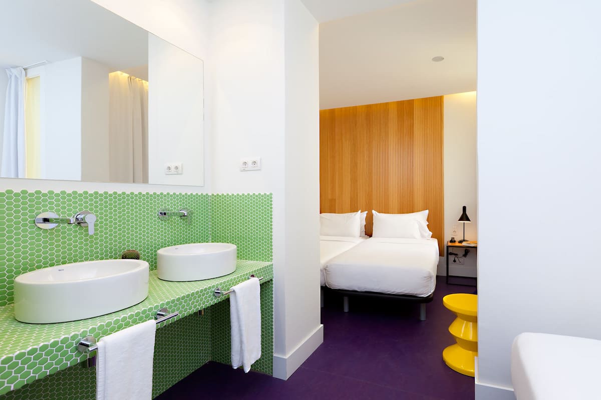 A modern bathroom with two sinks, a large mirror, and a bed with a wooden headboard.