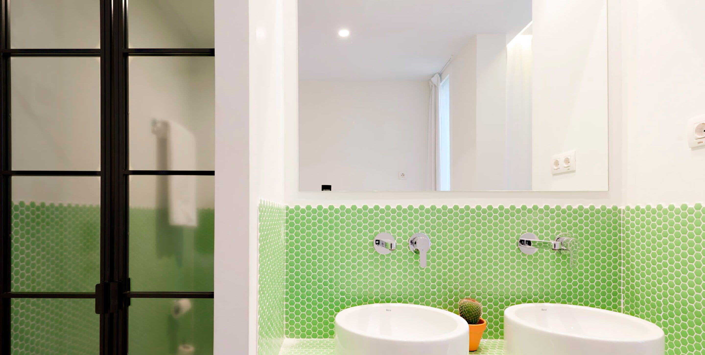 Un baño con dos lavamanos, un espejo y un salpicadero de azulejos hexagonales verdes.