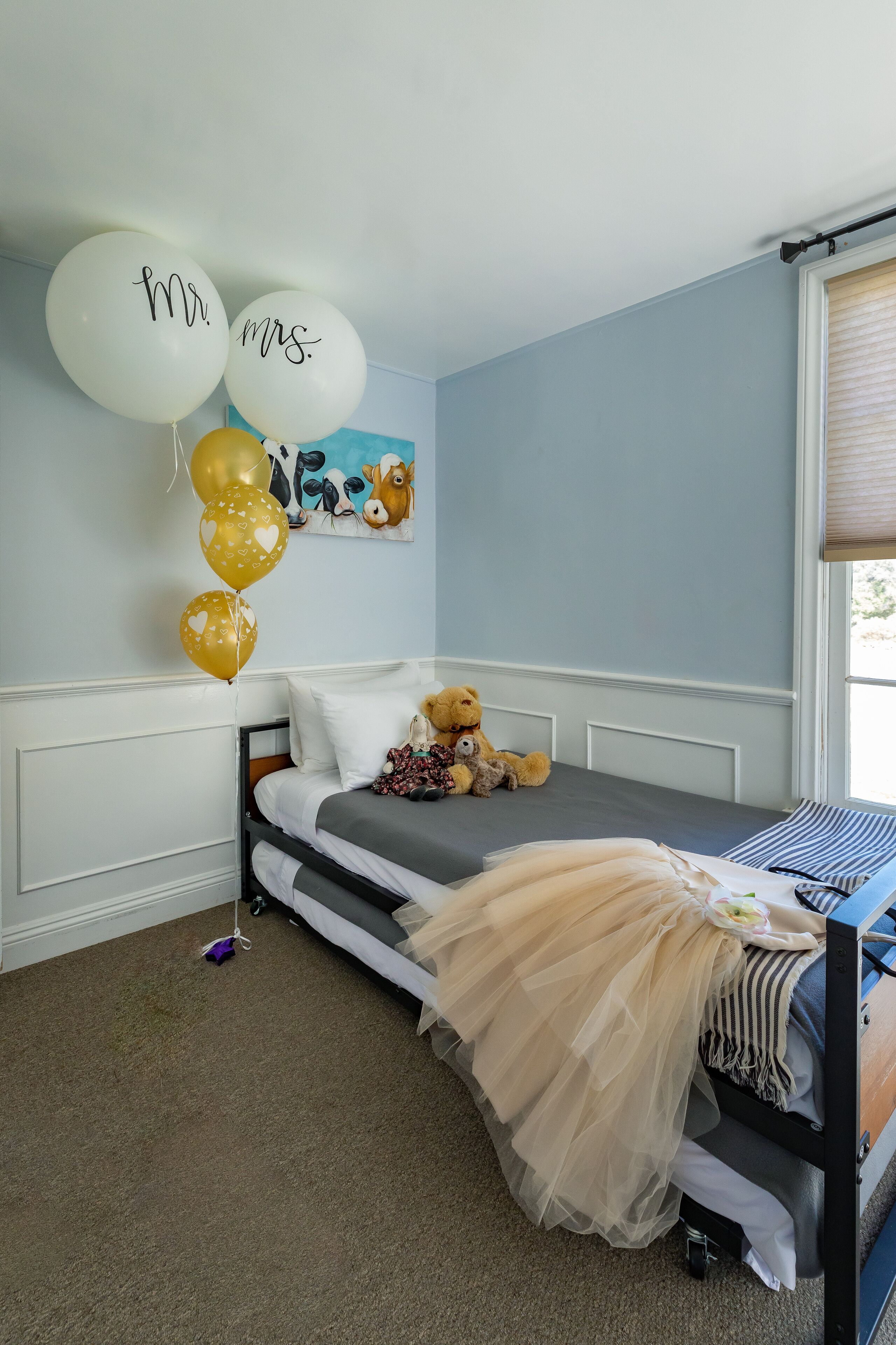 A bedroom with a bed, a teddy bear, balloons, and a painting on the wall.