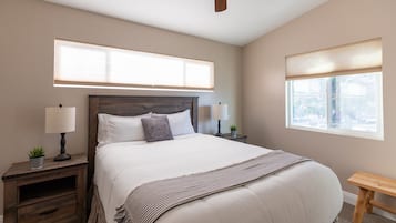 Un dormitorio con una cama grande, dos mesitas de noche con lámparas, un ventilador de techo y una ventana con persianas.