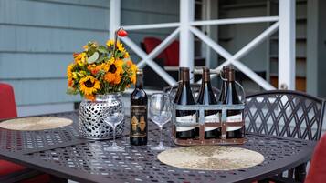 Una mesa metálica con un jarrón de girasoles, dos botellas de vino y dos copas de vino.