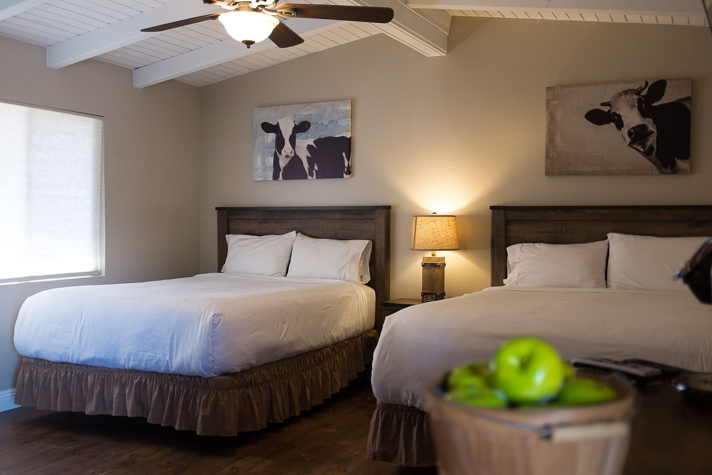 A hotel room with two beds, a ceiling fan, and artwork on the walls.